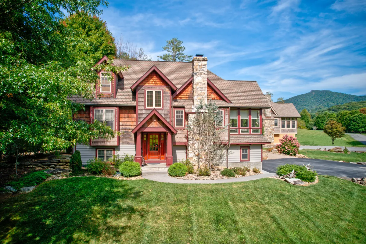 The image showcases the welcoming front entrance of a beautifully crafted single-family home, featuring a striking stone chimney, lush landscaping, and an inviting porch bathed in the golden light of sunset. The scene evokes a sense of warmth and comfort, perfect for family gatherings, outdoor barbecues, or simply unwinding while enjoying the natural beauty of the surroundings.