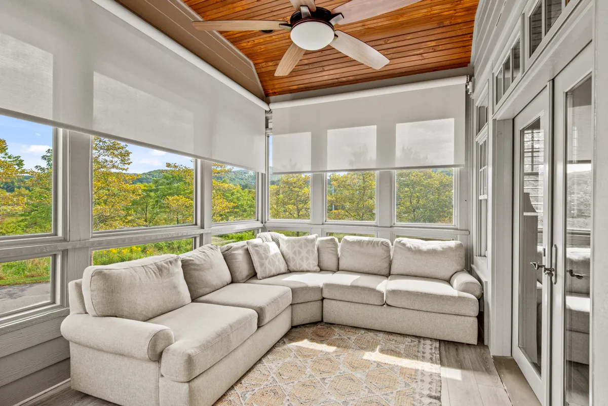 A large sectional sofa is arranged to encourage conversation, while oversized windows flood the space with mountain light and offer scenic views. The wooden ceiling fan and natural materials add to the cozy ambiance. This room is clearly designed for both socializing and peaceful relaxation.