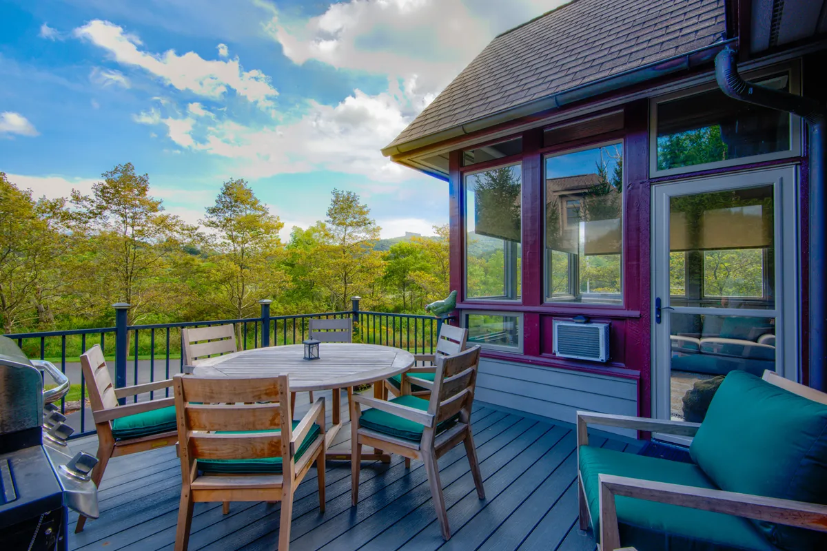 A round wooden table and chairs with green cushions are set on a patio, overlooking a scenic view of trees. The mood is serene, emphasizing outdoor dining, morning coffee, or evening gatherings—a perfect spot to unwind after enjoying local culinary experiences.