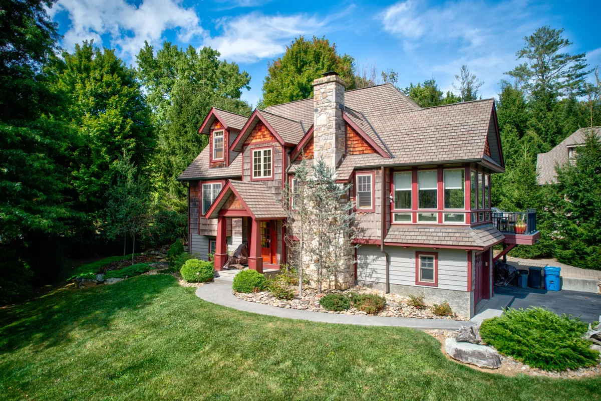 The home’s exterior is framed by a stone chimney, wooden accents, and lush greenery, with hints of a deck and landscaped paths. The setting suggests spaces for outdoor gatherings, sunset views, and seamless integration with nature—reinforcing the idea of adventure starting at home and continuing into the nearby trails and green spaces.