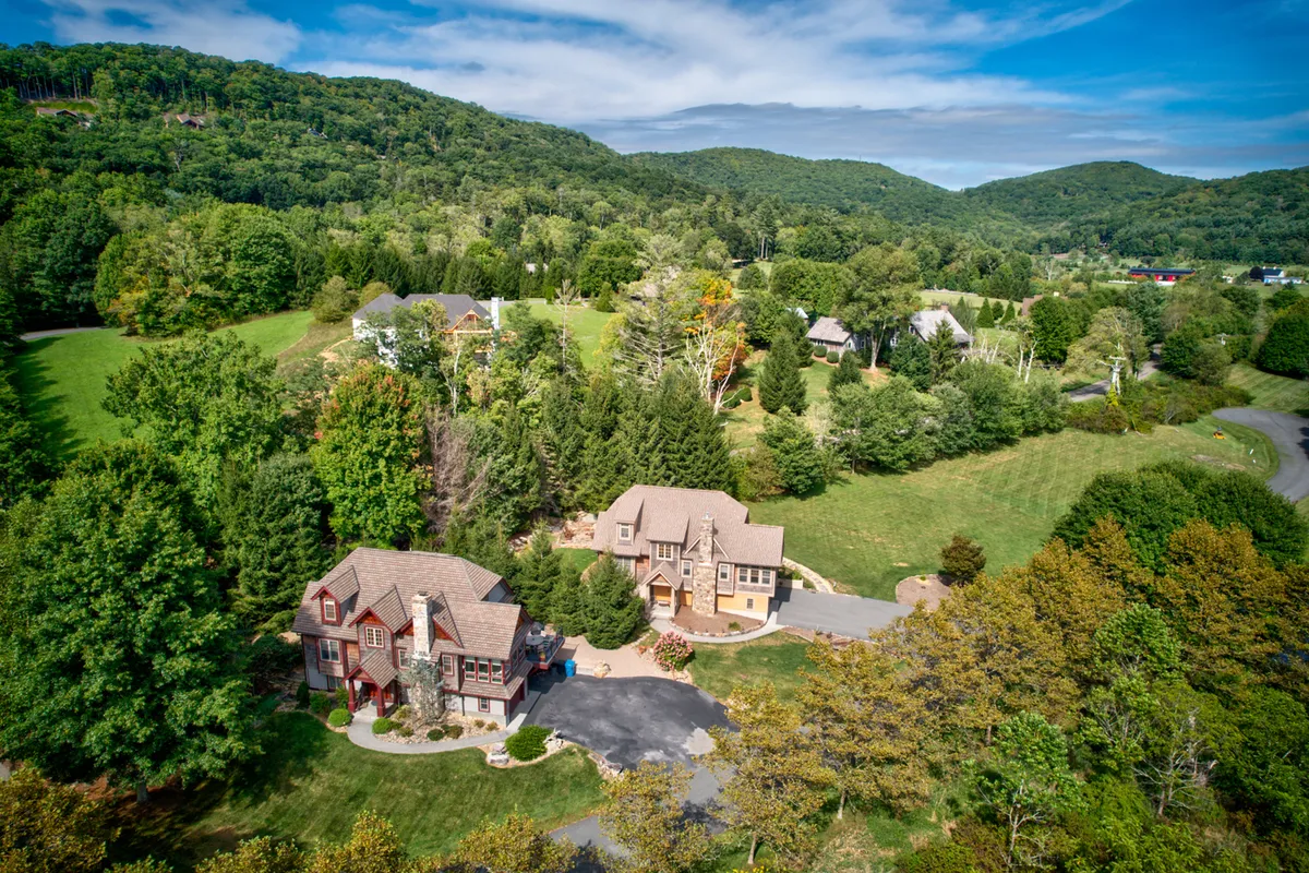 An inviting exterior shot featuring two distinct houses set against rolling hills and surrounded by lush greenery. The scene captures the tranquil, welcoming atmosphere of the area and hints at opportunities for outdoor activities and gatherings.
