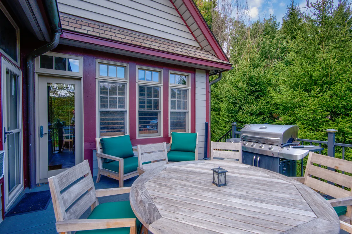 A spacious outdoor dining area features a large table with green chairs, a grill, and views into the home’s interior through large windows. The setup is ideal for group barbecues, outdoor meals, or celebrating special occasions in a casual, welcoming atmosphere.