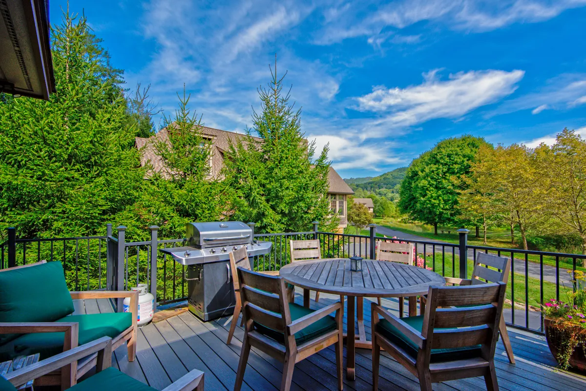 An expansive outdoor deck set against a backdrop of mountain views, furnished with a grill, dining table, and vibrant green chairs. The scene captures the spirit of al fresco dining, relaxation, and enjoying sunset or starry nights with friends and family.