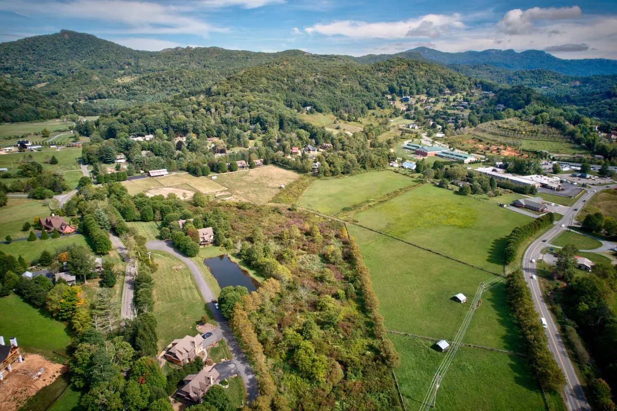 This wide-angle exterior view captures rolling hills, a serene pond, scattered homes, and farmland, suggesting abundant open space and immediate access to nature. The scene is peaceful, with visible walking paths around the pond and lush, inviting greenery. The context hints at the outdoor recreation opportunities available within close proximity.
