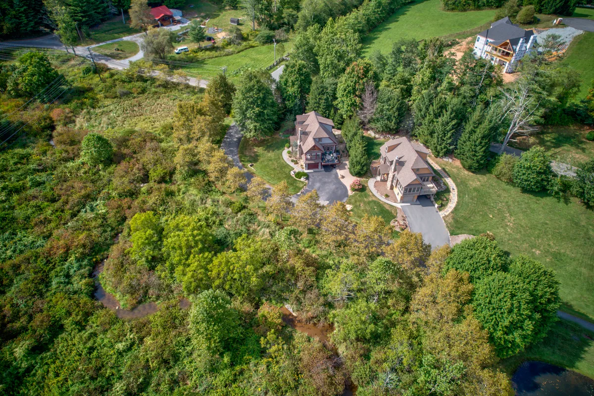 The photo displays two homes set amidst abundant greenery and a winding driveway, with the tranquil neighborhood extending into the background. The layout suggests a peaceful, low-traffic community, ideal for leisurely walks and outdoor activities with pets.