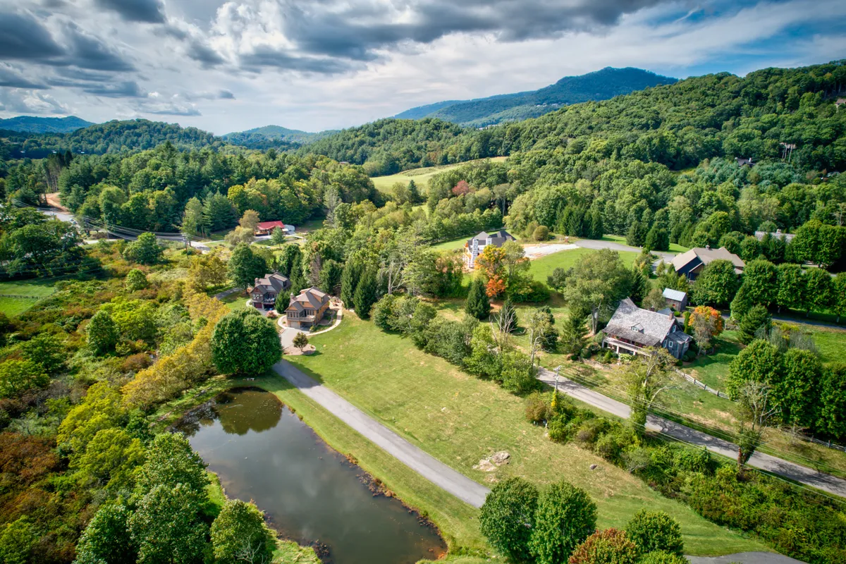 A tranquil view over rolling hills, a picturesque pond, wooded areas, and neighboring homes, inviting exploration of community amenities such as fishing, hiking, and picnicking. The scene is peaceful yet expansive, suggesting a world beyond the home’s immediate backyard.