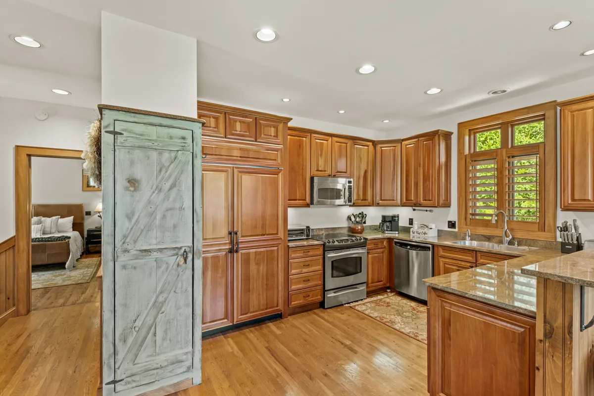 A close-up view of a spacious kitchen with wooden cabinetry, a kitchen island, and gleaming stainless steel appliances. The design feels warm and welcoming, with plenty of counter space and storage—ideal for both home chefs and casual cooks preparing hearty breakfasts or gourmet dinners.